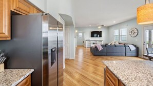 A modern kitchen with a stainless steel refrigerator, wooden cabinets, and granite countertops. - Fisherman`s Dream: Game Room & Walk to Beach (Surfside)