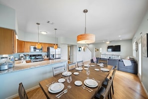 Una cocina moderna con armarios de madera, una isla central y un comedor preparado para seis personas con una mesa grande.