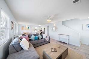 Una sala moderna con un sofá modular, una mesa de centro de madera y una escalera que sube a un nivel superior.