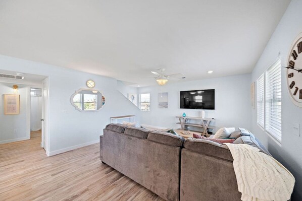 A spacious living room with a large sectional sofa, a flat-screen TV mounted on the wall, and a staircase leading to an upper level.