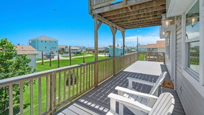 Une terrasse en bois avec une balustrade, une chaise Adirondack blanche et une vue sur un quartier résidentiel avec des maisons et un ciel bleu dégagé.
