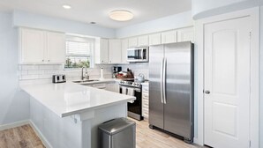 Une cuisine moderne avec des meubles blancs, des appareils en acier inoxydable et un grand îlot central.