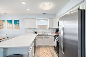 A modern kitchen with white cabinets, a stainless steel refrigerator, and a large island.