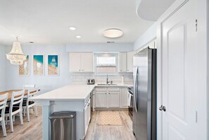 Eine moderne Küche mit weißen Schränken, einem Edelstahlkühlschrank und einem Essbereich mit Holzstühlen und einem weißen Tisch.