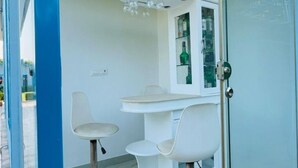 A room with a white table and two white chairs, a glass door, and a small window with a view. - Cozy 2-bedroom farmhouse in awesome Noida with AC, WiFi (Noida)