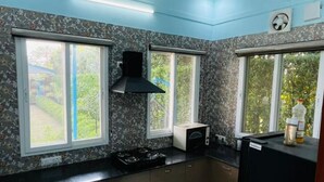 A kitchen with two windows, a black range hood, and a black refrigerator. - Cozy 2-bedroom farmhouse in awesome Noida with AC, WiFi (Noida)