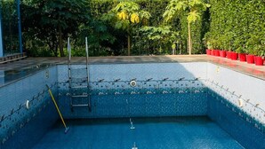 A swimming pool with a ladder, a mop, and a pool brush. - Cozy 2-bedroom farmhouse in awesome Noida with AC, WiFi (Noida)