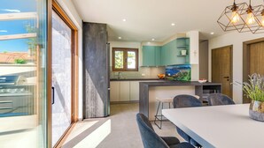 A modern kitchen with a large island, a dining area with a white table, and a view through a glass door. - Casa del Mare... Quiet location... spacious swimming pool... relaxing vacation. (Lakmartin)