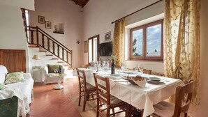 Comedor con una mesa para cuatro, un sofá, una escalera y una ventana con cortinas.