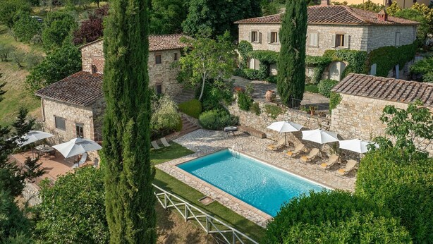 Una villa de piedra con piscina, mobiliario exterior y abundante vegetación.