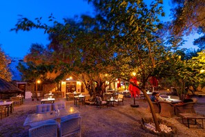 An outdoor dining area with tables and chairs, surrounded by trees and a building with lights. - guesthouse by west (Datca)