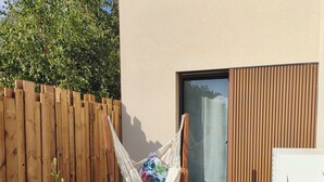 Un fauteuil suspendu dans un coin du jardin, avec une clôture en bois, un petit rocher et un cactus.