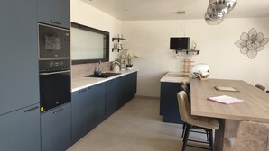 Une cuisine moderne avec des meubles de couleur sombre, un four encastré et un coin repas comprenant une table et des chaises en bois.