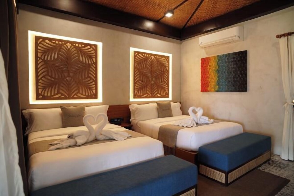 Une chambre d’hôtel avec deux lits, un banc bleu, des panneaux muraux décoratifs et une peinture abstraite aux couleurs vives.