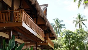 Hotel con balcón de techo de paja, barandillas de madera y vistas a palmeras.