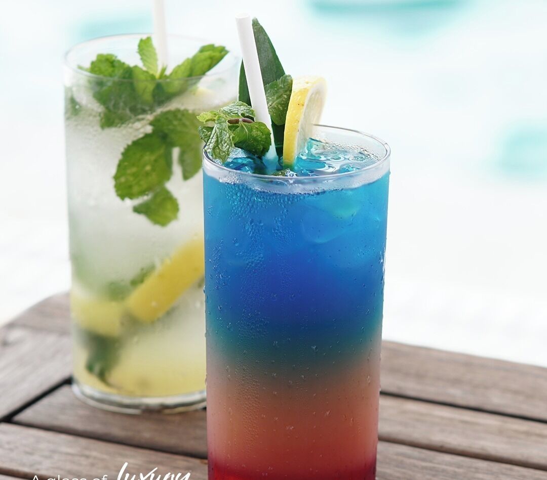 Two glasses of iced drinks with mint leaves and lemon slices, placed on a wooden surface.