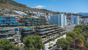 Un moderno complesso alberghiero con diversi edifici, giardini sui tetti e una vista aperta sulle colline circostanti.