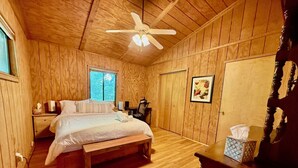 Camera da letto con pannelli in legno, un letto, una scrivania, una sedia, una ventola a soffitto e una finestra.