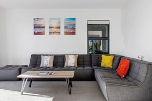 A modern living room with a grey sectional sofa, a wooden coffee table, and three wall-mounted paintings. - Idyllic Getaway - stylish and relaxing getaway with private spa (Taupō)
