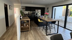 A modern kitchen with a central island, a dining area with a wooden table, and a large sliding glass door leading to an outdoor patio. - Villa with pool Pessac between Bordeaux and Bassin d'Arcachon (Pessac)