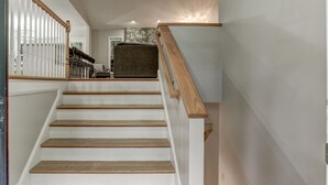 A staircase with wooden steps and a wooden handrail, leading to a landing with a stone wall and a gray sofa.