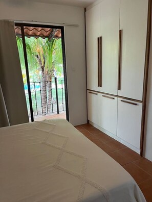 A bedroom with a bed, a sliding glass door leading to a balcony with a palm tree, and a white wardrobe with two drawers. - Beautiful Dolce Vita Retreat (Sardinal de Carrillo)