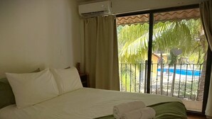 Ein Hotelzimmer mit Bett, grüner Decke und Blick auf einen Pool durch eine Schiebetür.