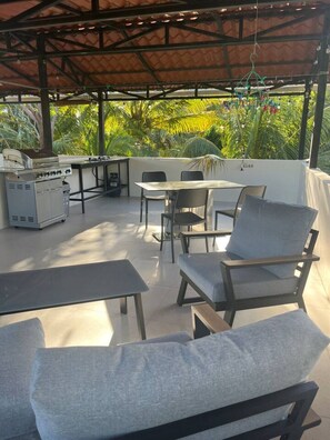 An outdoor patio with a grill, seating area, and a view of greenery. - Beautiful Dolce Vita Retreat (Sardinal de Carrillo)
