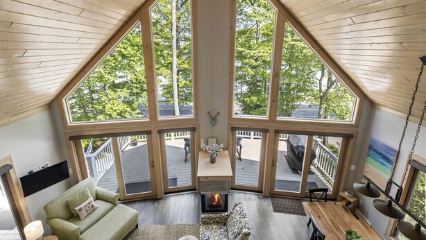 A loft-style room with a large skylight, a fireplace, and a view of a deck and trees. - Attitude Adjustment on Glen Lake (Glen Arbor)