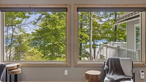 A room with two large windows, a wooden chair, a small wooden stool, and a thermostat on the wall. - Attitude Adjustment on Glen Lake (Glen Arbor)