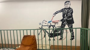 A room with a green metal crib, a brown bean bag chair, and a wall mural of a man riding a bicycle.
