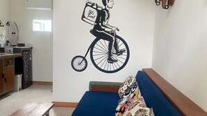 A living room with a blue sofa, a wall-mounted bicycle illustration, and a small table with a chair.