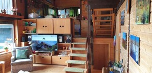 A cozy cabin interior with wooden walls, a television, a sofa, and a staircase. - Holiday Home 'Bernau13, Rechbergblick' with Mountain View, Shared Garden and Wi-Fi (Bernau im Schwarzwald)