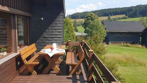 A wooden deck with a table and benches, overlooking a green landscape with buildings. - Holiday Home 'Bernau13, Rechbergblick' with Mountain View, Shared Garden and Wi-Fi (Bernau im Schwarzwald)