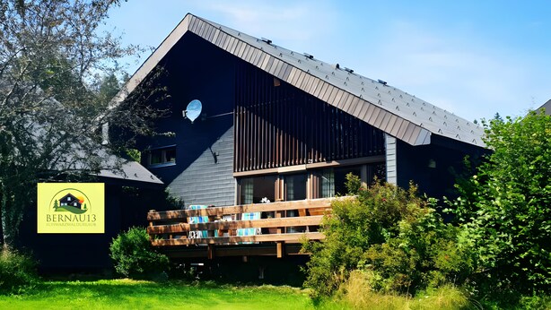 A modern building with a sloped roof, a wooden deck, and a sign indicating it is a hotel named 'Bernau13.' - Holiday Home 'Bernau13, Rechbergblick' with Mountain View, Shared Garden and Wi-Fi (Bernau im Schwarzwald)