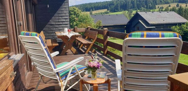 A wooden deck with outdoor furniture, a table, and a view of a lake and buildings in the background. - Holiday Home 'Bernau13, Rechbergblick' with Mountain View, Shared Garden and Wi-Fi (Bernau im Schwarzwald)