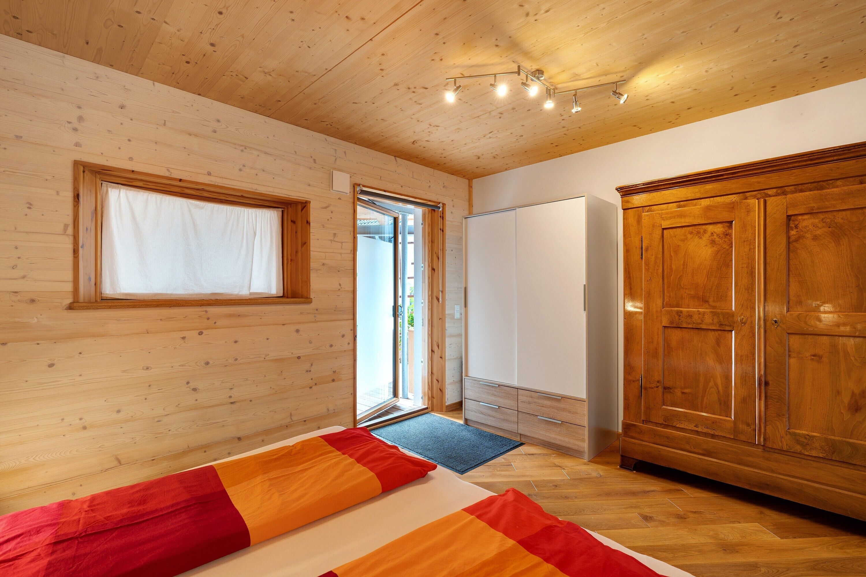 Habitación con paneles de madera, una cama, un armario y una puerta que da al exterior.