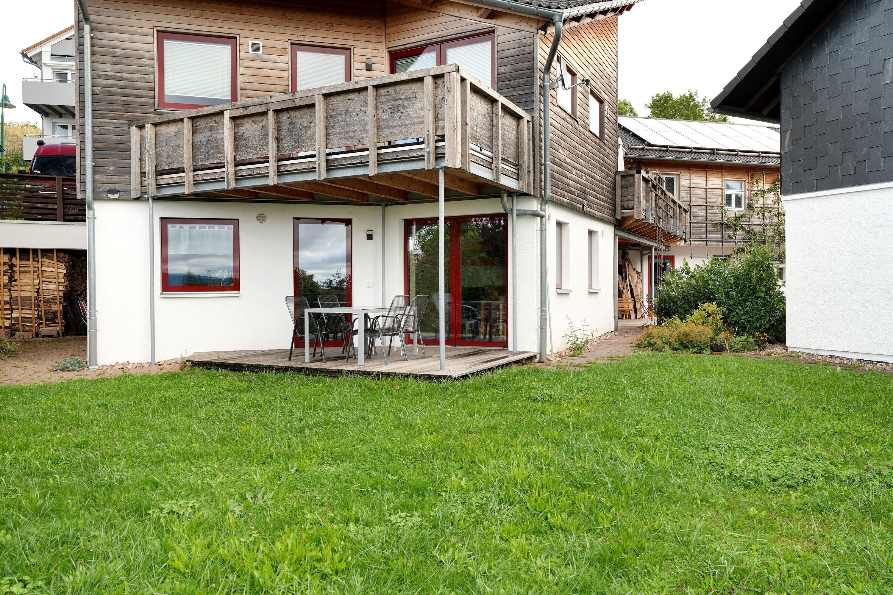 Una casa de dos pisos con un balcón, un patio con mobiliario exterior y un césped bien cuidado.