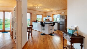 Una cocina moderna con suelo de madera, una isla central con taburetes de bar, un refrigerador y vistas al exterior.