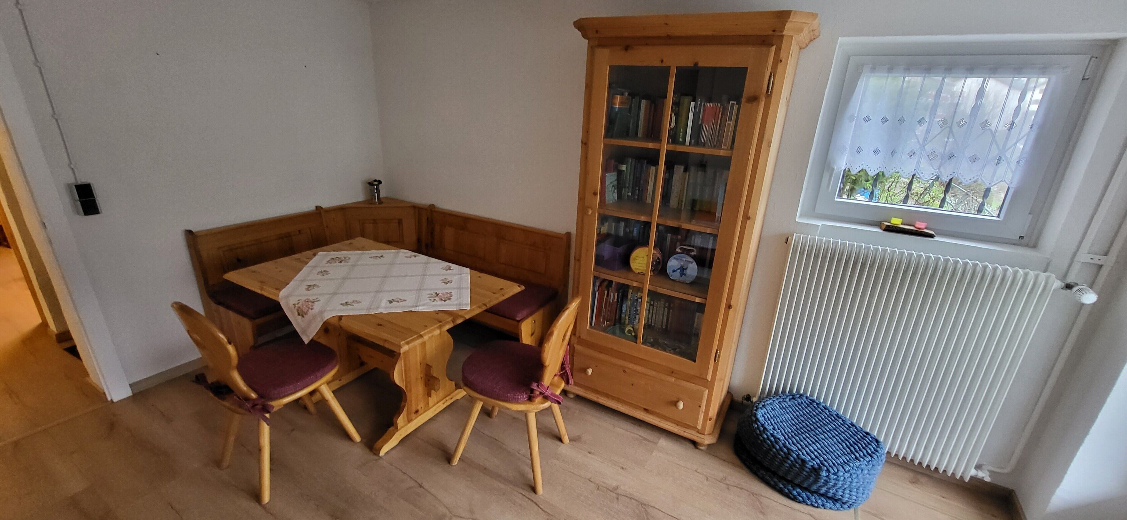 A room with a wooden table and chairs, a bookshelf, a radiator, and a window with a view.