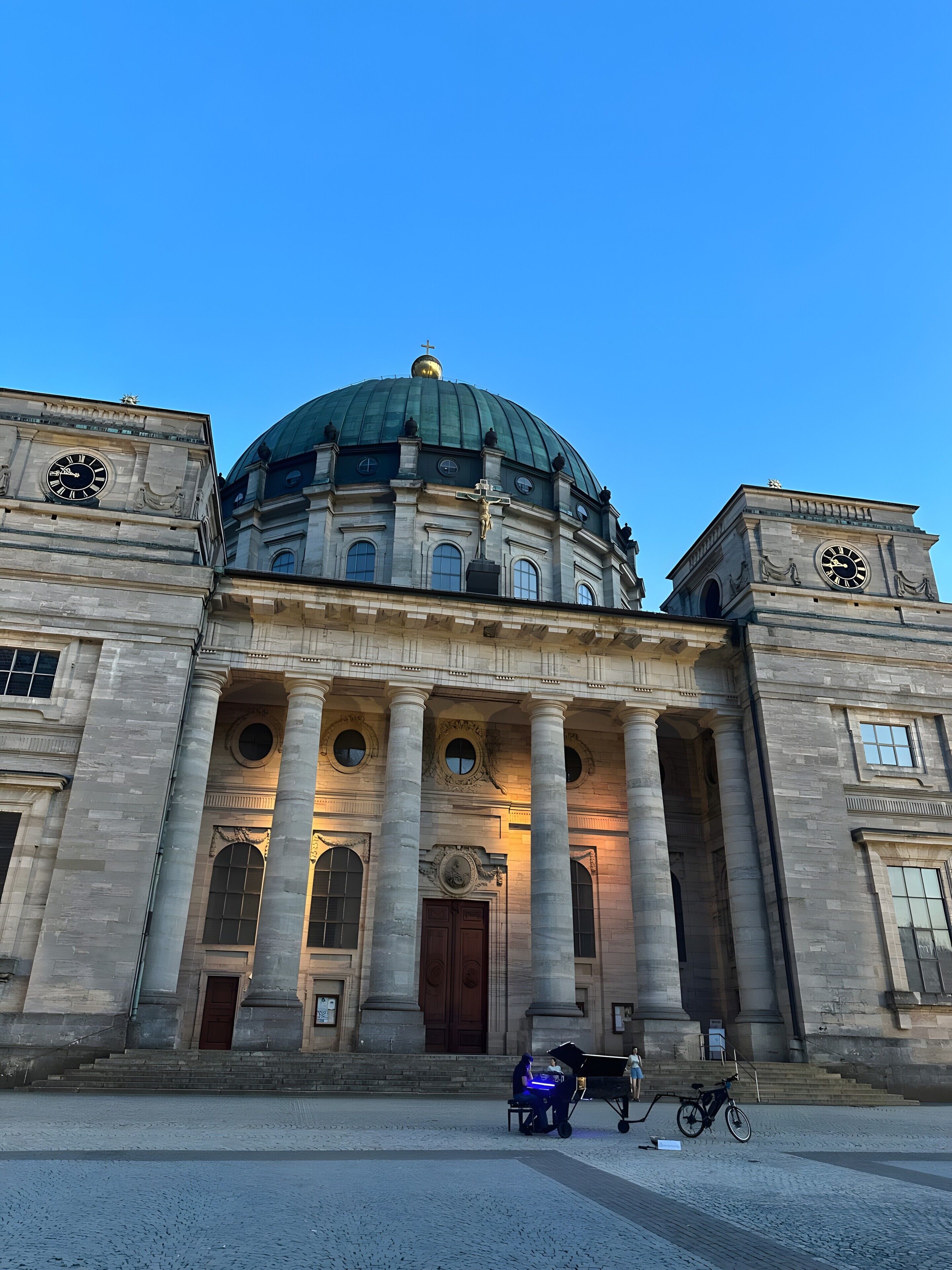 A large building with a prominent dome and two clock towers, featuring classical architecture with columns and arched windows.