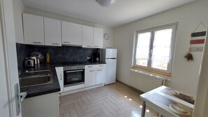 A kitchen with white cabinets, a black countertop, a stove, a refrigerator, and a window with a view.
