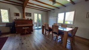 A room with a piano, a dining table with chairs, and a large window.