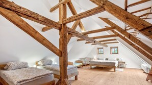 A high-ceilinged room with exposed wooden beams, a loft bed, a smaller bed, and a crib. - Apartment 'Hochwald' with Mountain View and Wi-Fi (Bertsdorf-Hörnitz)
