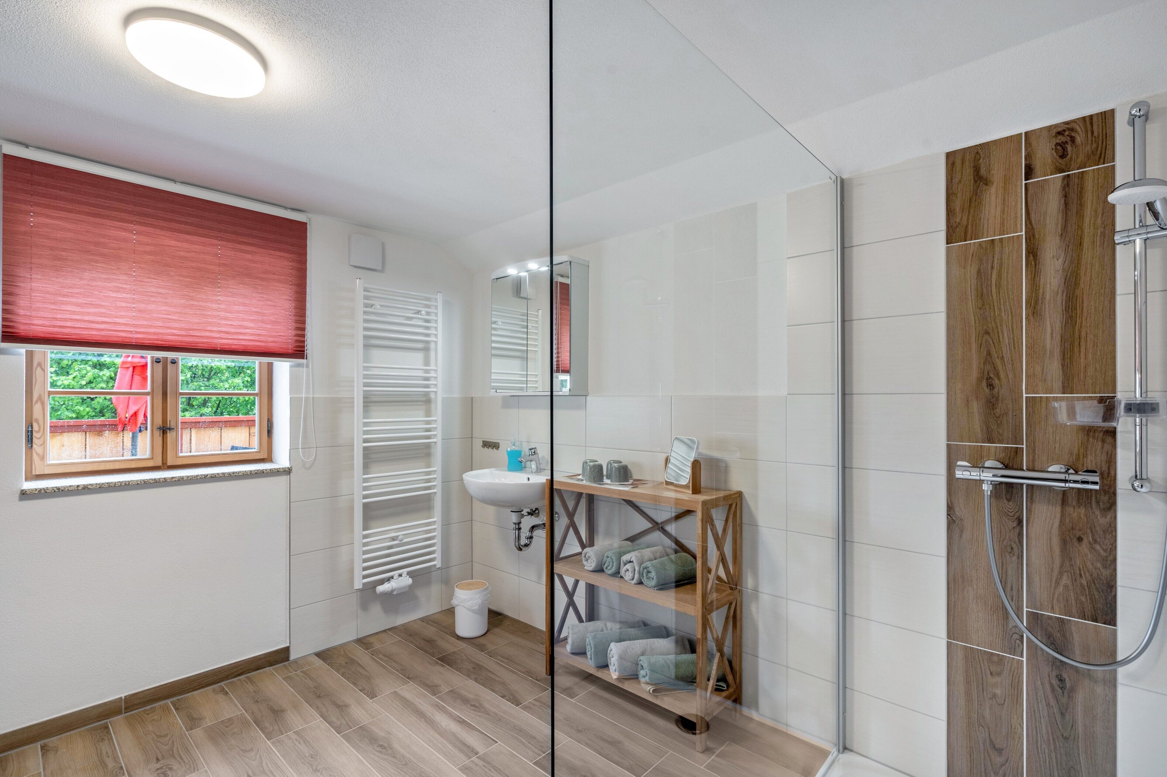 Un baño moderno con cabina de ducha de vidrio, tocador de madera y ventana con persianas.