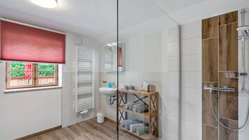 Un baño moderno con cabina de ducha de vidrio, tocador de madera y ventana con persianas.