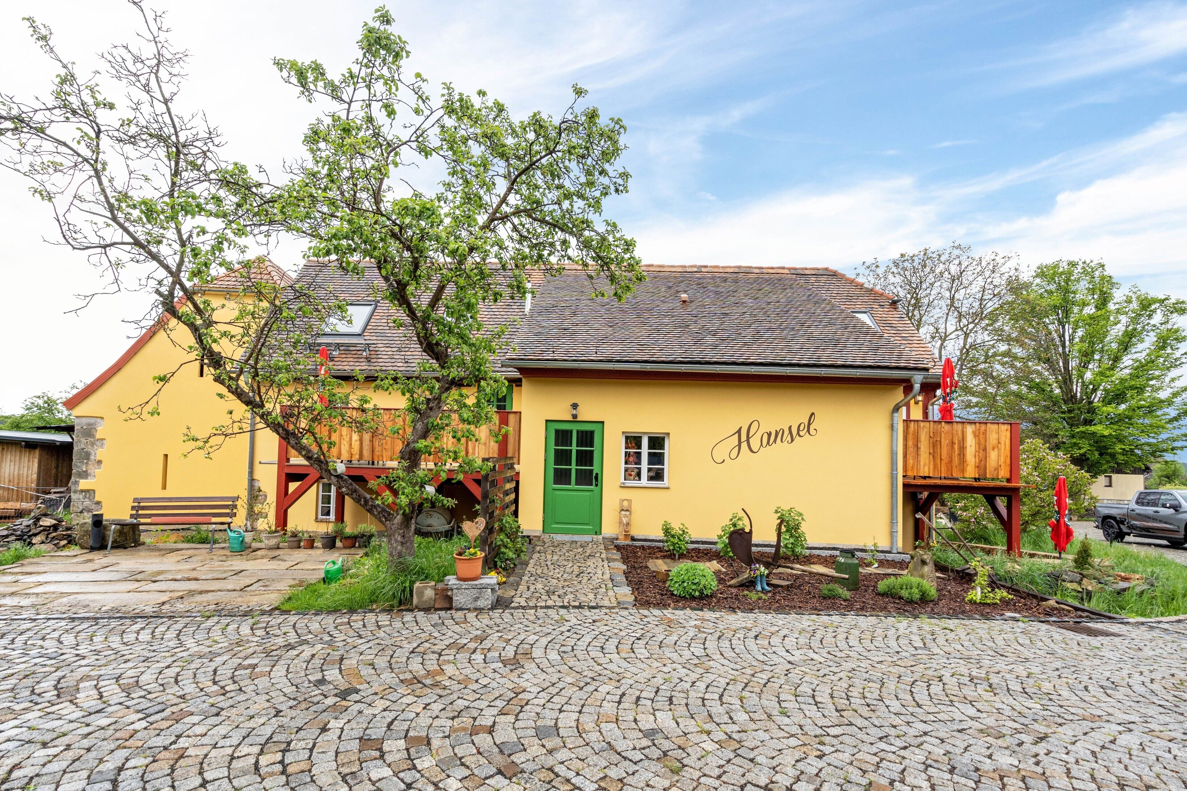 En gul byggnad med en grön dörr, en namnskylt med texten ”Hansel”, och en innergård med kullerstenar.