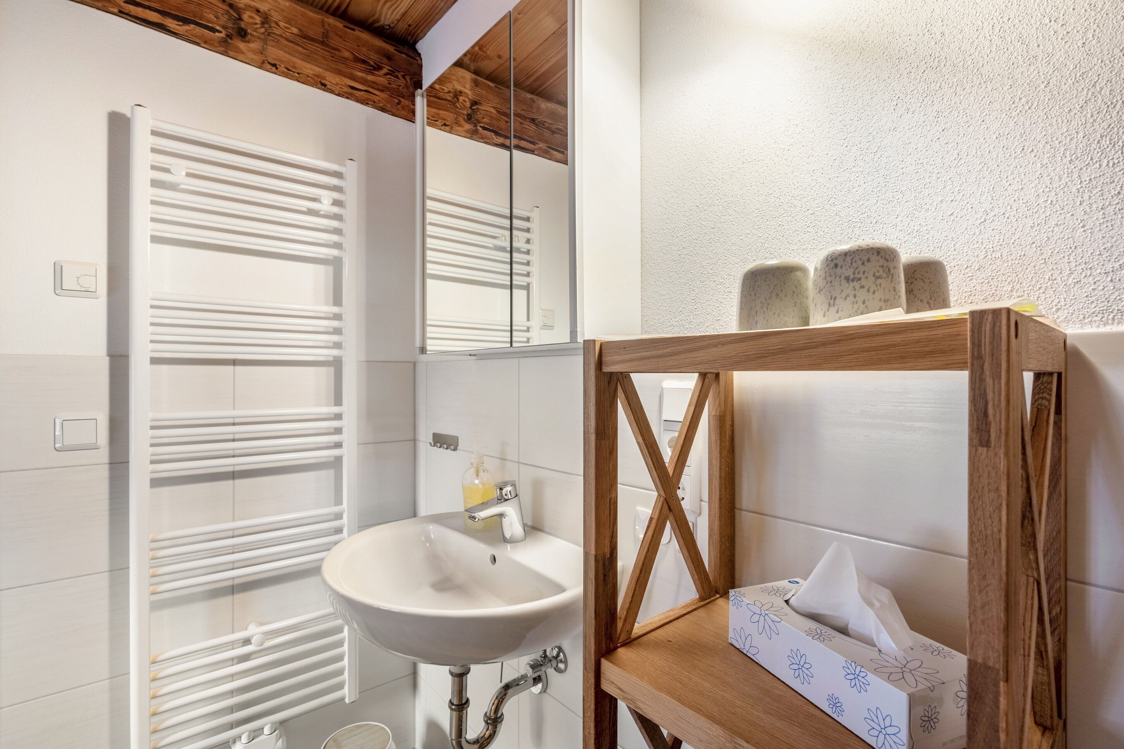 Un bagno con un lavandino bianco, un portasciugamani e una mensola in legno con un pacco di fazzoletti.
