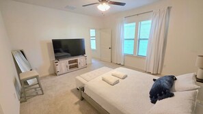 A bedroom with a bed, a television, a ceiling fan, and a window with curtains.