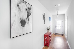 Un couloir avec un grand tableau encadré représentant un cheval, une console rouge et une porte blanche au fond.